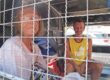 Two foreign overstayers sitting behind the mesh of a police truck in Phuket.