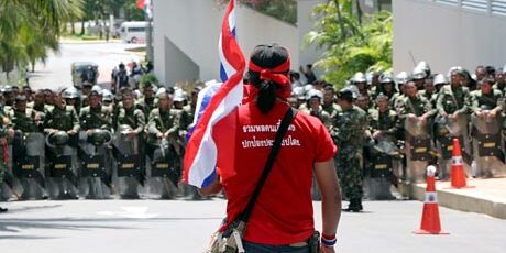 red shirts Red Shirt protester carrying a Thai flag in front of a line of soldiers during the 2010 Bangkok demonstrations.