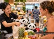 Illustration of a friendly supermarket checkout interaction involving two panda plush toys in Thailand.