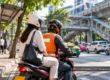 Helmeted motorcycle taxi driver carrying a helmeted passenger on a busy Bangkok street