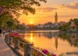 AI-generated conceptual scenery inspired by Roi Et: a lakeside promenade at sunset with a pavilion island and a tall golden standing Buddha above the town (not a photograph of a real place)