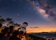 Students observing the night sky through a large telescope above misty Thai mountains.