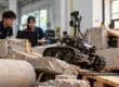 Student robotics team testing a tracked rescue robot on a simulated rubble course in an engineering laboratory.