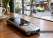 A silver and black 2000s keypad mobile phone on a cafe table, with a blurred Thai city street outside.