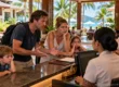Frustrated tourist family complaining at a resort reception desk in Phuket while staff listen with blank faces. AI-generated image.