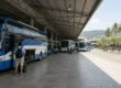 Traveller with a backpack keeping hold of his suitcase beside a blue and white coach at a covered bus station in Pattaya, with passengers waiting further along the platform. AI-generated image.