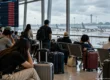 Airport departure board showing cancelled flights while stranded passengers with luggage wait beside grounded aircraft. AI-generated image.
