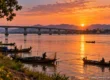 The Mekong river at Nong Khai at sunset with the bridge to Laos and fishermen in longtail boats. AI-generated image.